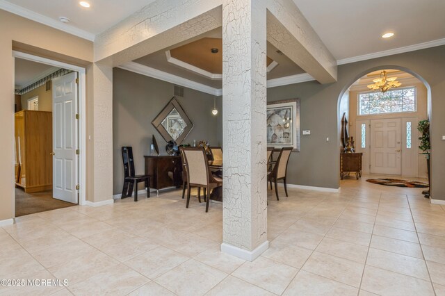 foyer featuring a chandelier, light tile patterned floors, crown molding, arched walkways, and baseboards