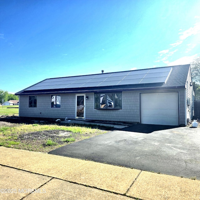 single story home with an attached garage, solar panels, asphalt driveway, and a shingled roof