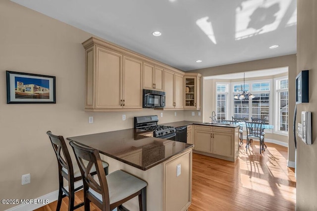 kitchen featuring black appliances, a peninsula, dark countertops, a chandelier, and cream cabinets
