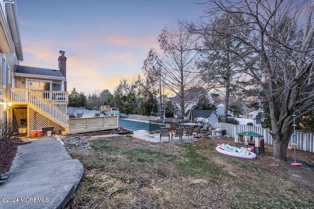 yard at dusk with fence, a wooden deck, a patio area, and stairs