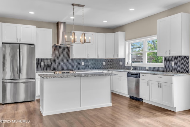 kitchen with stainless steel appliances, wall chimney exhaust hood, a center island, light stone counters, and recessed lighting