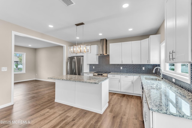kitchen featuring stainless steel appliances, wall chimney exhaust hood, light wood-style flooring, decorative backsplash, and a sink