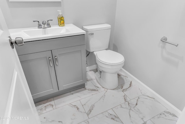 half bathroom featuring baseboards, marble finish flooring, vanity, and toilet
