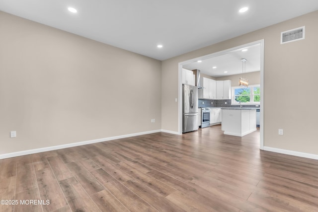 unfurnished living room with wood finished floors, a sink, recessed lighting, and baseboards