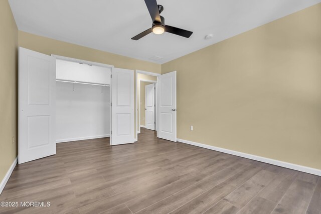 unfurnished bedroom featuring wood finished floors, baseboards, a closet, and a ceiling fan
