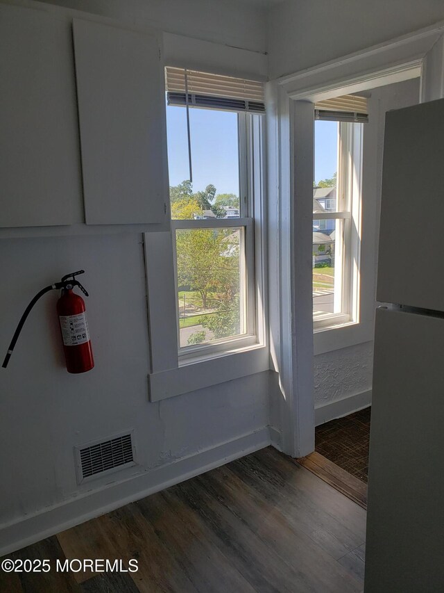 detailed view of freestanding refrigerator, a fire extinguisher, baseboards, and wood finished floors