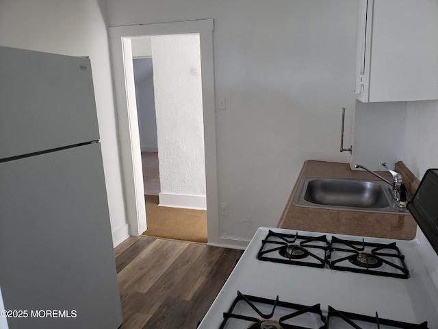 kitchen with freestanding refrigerator, a sink, dark wood-style flooring, white cabinets, and baseboards