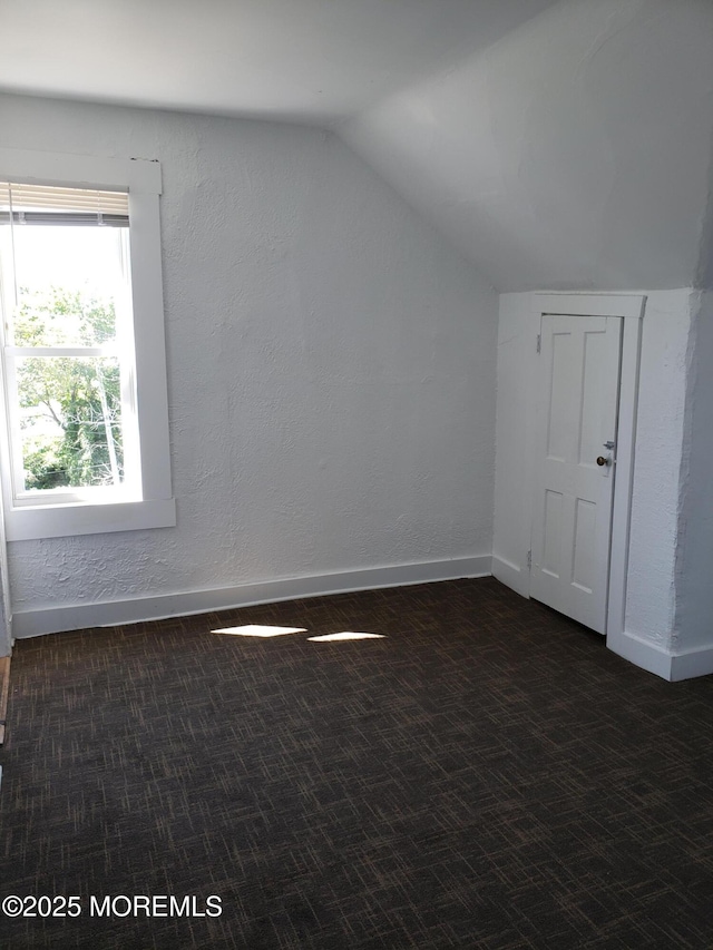 additional living space with dark carpet, vaulted ceiling, baseboards, and a textured wall