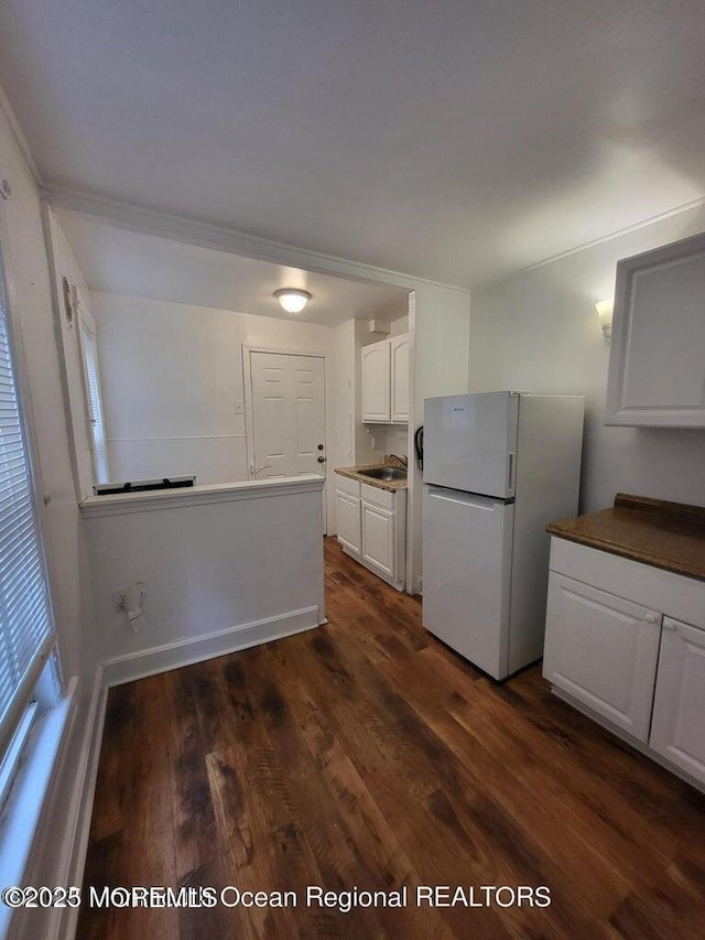 kitchen featuring freestanding refrigerator, a sink, white cabinetry, and dark wood-style floors
