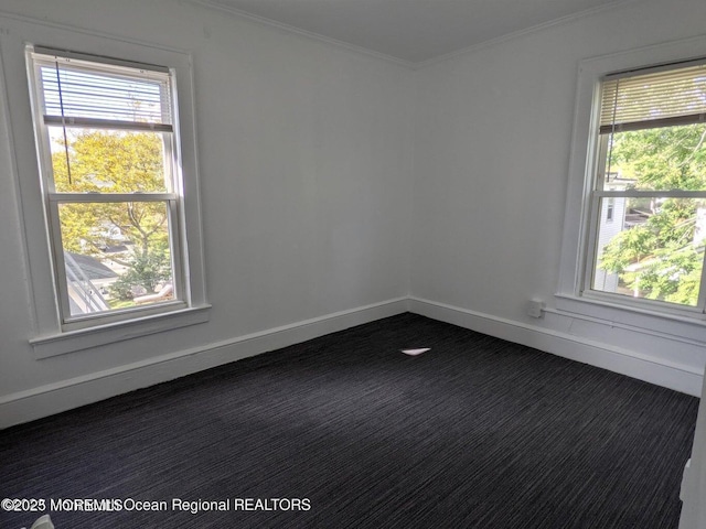 unfurnished room featuring dark carpet, healthy amount of natural light, crown molding, and baseboards
