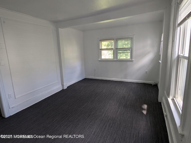 spare room featuring baseboards and dark colored carpet