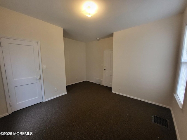 unfurnished room featuring dark carpet and baseboards