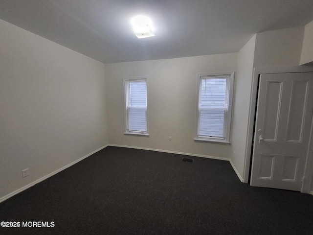 spare room featuring dark carpet and baseboards