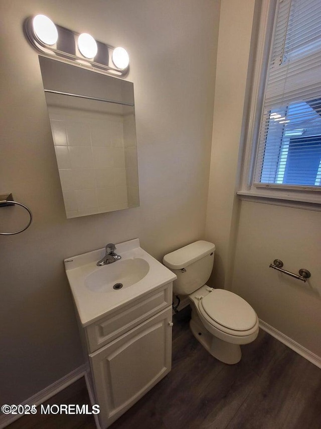 half bath with wood finished floors, toilet, vanity, and baseboards