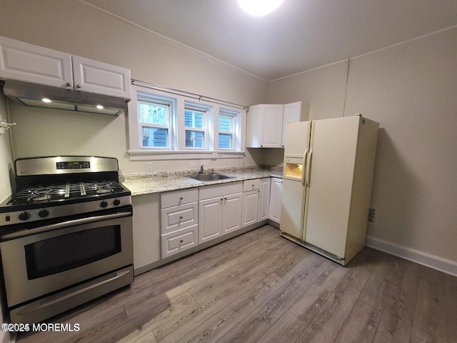 kitchen featuring stainless steel gas stove, white refrigerator with ice dispenser, under cabinet range hood, a sink, and light wood finished floors