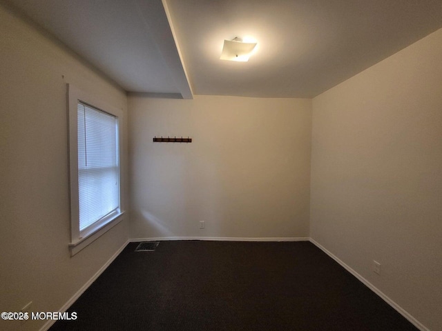 unfurnished room featuring dark colored carpet and baseboards
