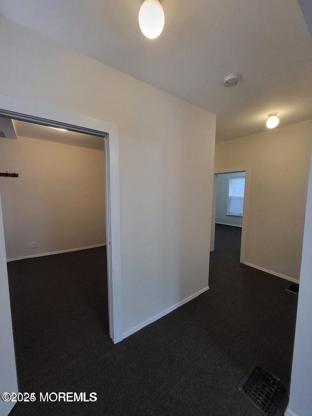 corridor featuring dark carpet and baseboards
