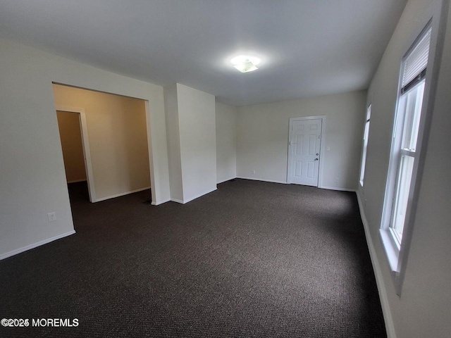 unfurnished room featuring baseboards and dark carpet