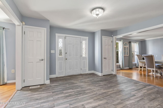 entryway featuring wood finished floors, baseboards, and crown molding