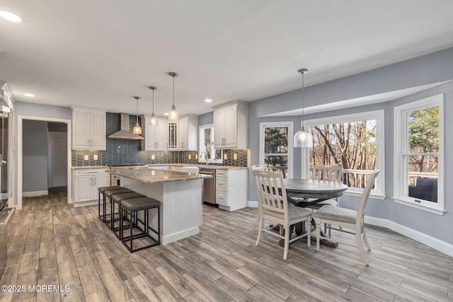 kitchen featuring wall chimney range hood, dishwasher, decorative backsplash, a kitchen island, and recessed lighting