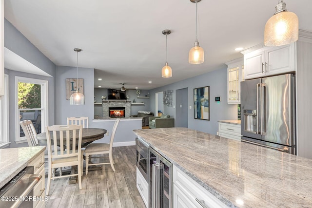 kitchen featuring appliances with stainless steel finishes, light wood finished floors, a stone fireplace, beverage cooler, and recessed lighting