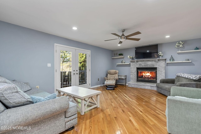 living area featuring a ceiling fan, french doors, light wood finished floors, a brick fireplace, and recessed lighting