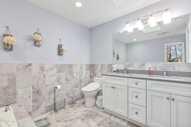 full bath featuring tile walls, toilet, marble finish floors, double vanity, and wainscoting