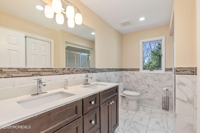 full bath with tile walls, marble finish flooring, double vanity, toilet, and a shower with shower door