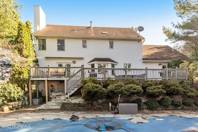 back of property featuring stairway, a wooden deck, a chimney, a shingled roof, and a covered pool
