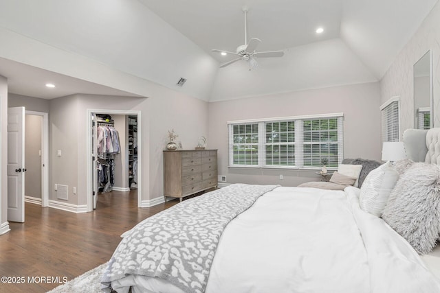 bedroom with dark wood-type flooring, lofted ceiling, a walk in closet, baseboards, and recessed lighting