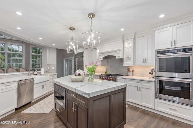 kitchen featuring built in appliances, a sink, backsplash, a chandelier, and white cabinets