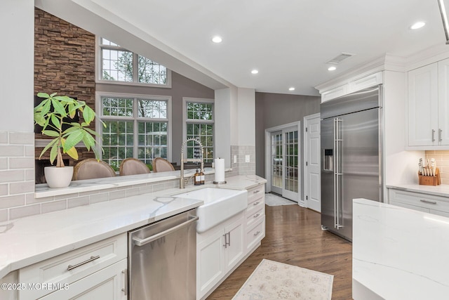 kitchen with appliances with stainless steel finishes, a sink, dark wood-type flooring, decorative backsplash, and light stone countertops