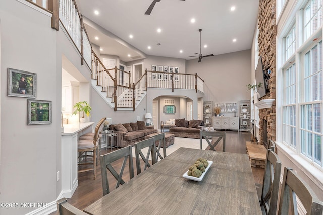 dining space with a ceiling fan, a towering ceiling, wood finished floors, arched walkways, and a stone fireplace