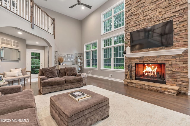 living room with a ceiling fan, a stone fireplace, wood finished floors, a towering ceiling, and arched walkways