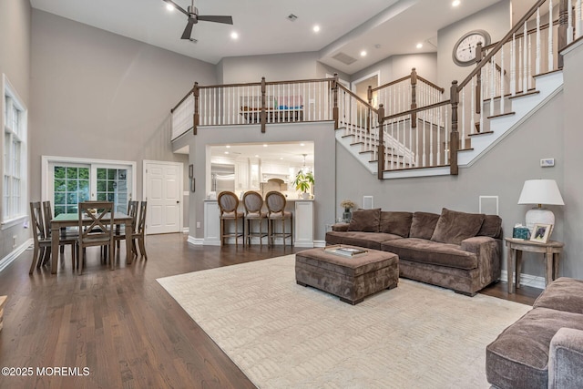 living room featuring dark wood finished floors, ceiling fan, a towering ceiling, stairs, and recessed lighting