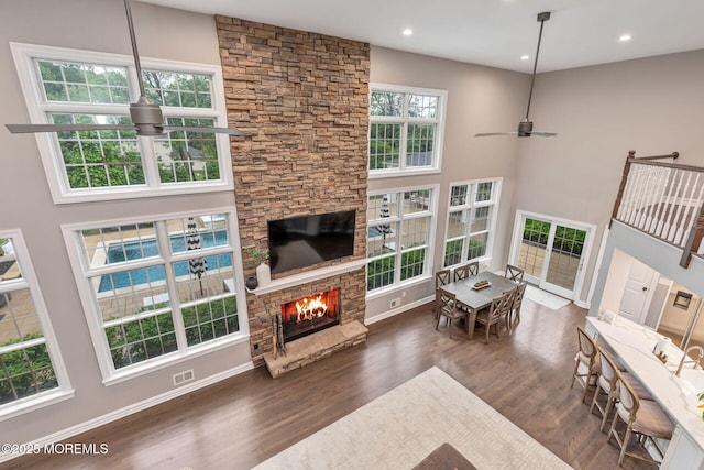 living room with a ceiling fan, wood finished floors, a stone fireplace, baseboards, and a high ceiling