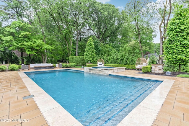 view of pool featuring an outdoor living space, a patio area, a pool with connected hot tub, and view of scattered trees