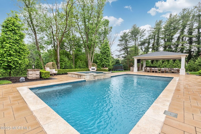 view of pool with a gazebo, a patio, a pool with connected hot tub, and view of scattered trees