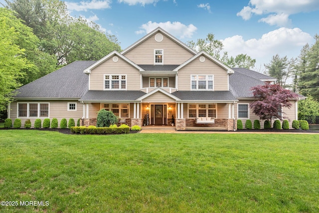view of front of house with stone siding, a porch, a front yard, and roof with shingles