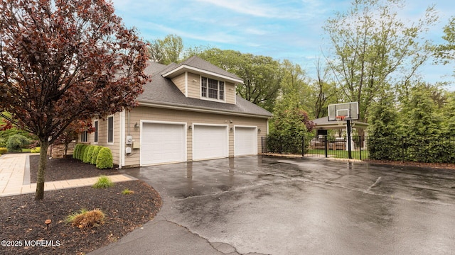 view of side of property with asphalt driveway, fence, and roof with shingles