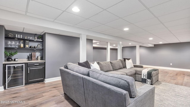 living area featuring beverage cooler, bar, light wood finished floors, baseboards, and a paneled ceiling