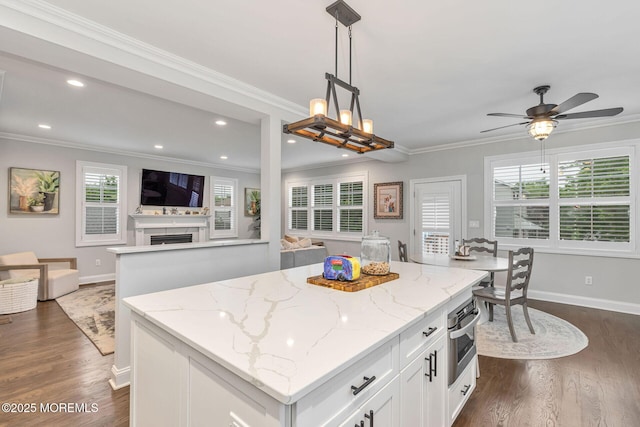 kitchen featuring open floor plan, a center island, baseboards, white cabinetry, and crown molding