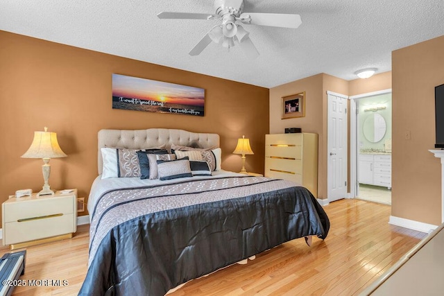 bedroom featuring wood finished floors, a textured ceiling, ensuite bath, baseboards, and ceiling fan