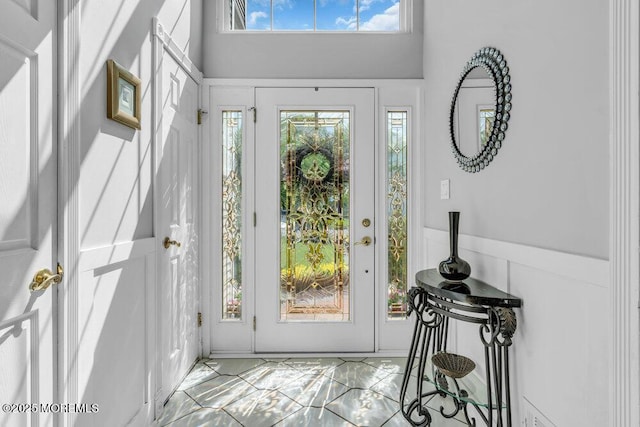 foyer featuring healthy amount of natural light, marble look tile flooring, and a towering ceiling
