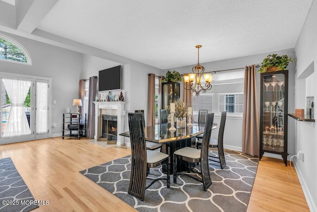 dining room with wood finished floors, a chandelier, baseboards, a high end fireplace, and a textured ceiling