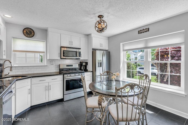 kitchen with appliances with stainless steel finishes, a sink, backsplash, dark countertops, and a textured ceiling
