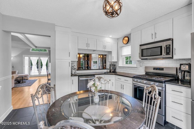 kitchen featuring appliances with stainless steel finishes, dark countertops, white cabinets, dark tile patterned floors, and a textured ceiling