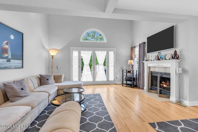 living area featuring wood finished floors, a high end fireplace, beam ceiling, a high ceiling, and baseboards