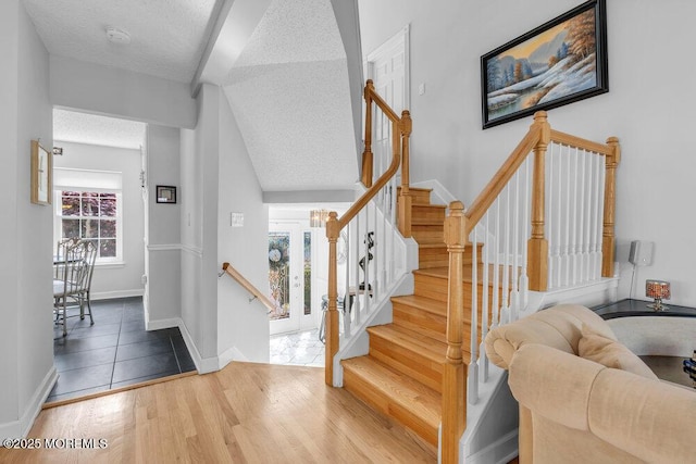stairs featuring a textured ceiling, wood finished floors, baseboards, and vaulted ceiling