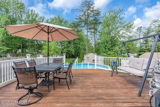 wooden terrace featuring a shed, outdoor dining area, an outdoor structure, view of wooded area, and fence